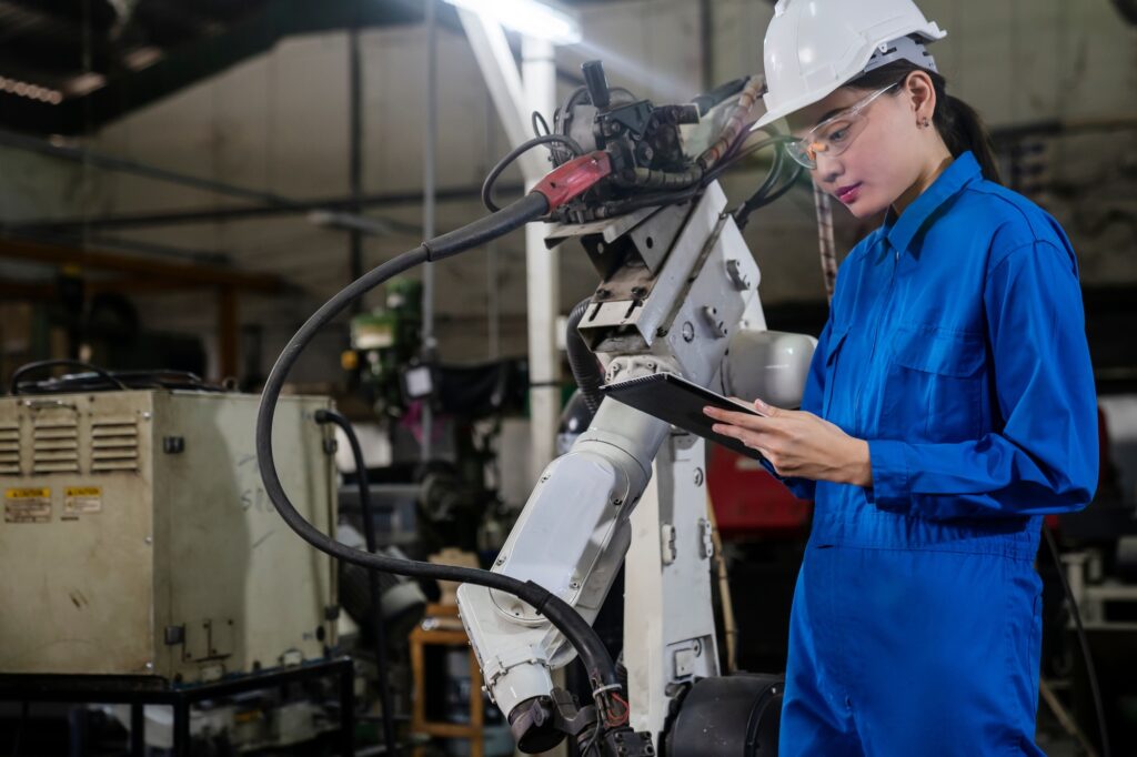 Woman engineering control robot arm in factory.